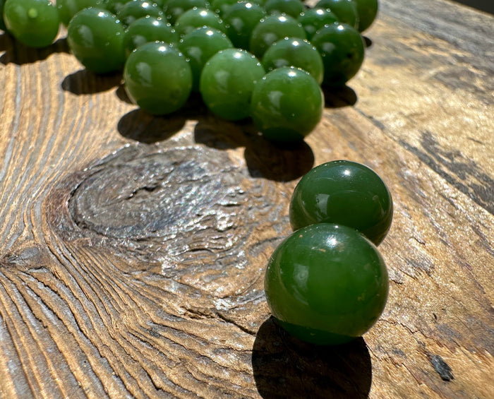 Two glossy green jade beads in the foreground on a textured wooden surface with more beads in the background