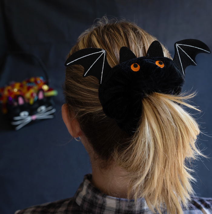Person wearing a black bat-shaped hair accessory with orange eyes on a dark background