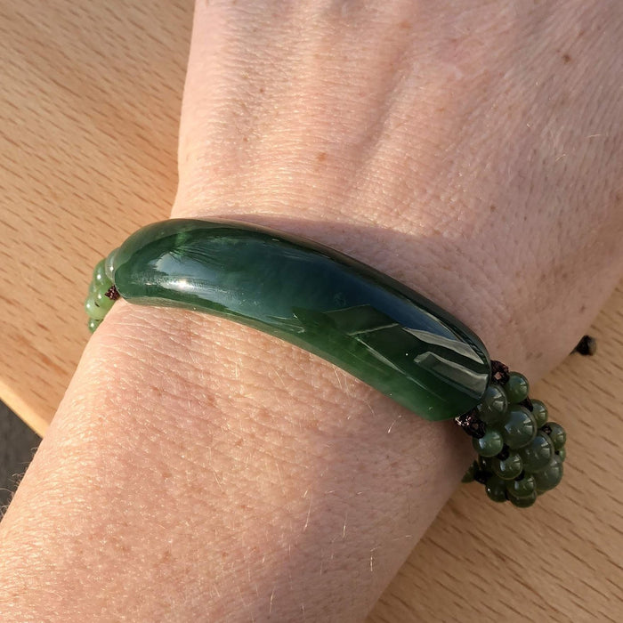 Green bracelet with a large curved central stone and multiple green bead accents worn on the wrist.