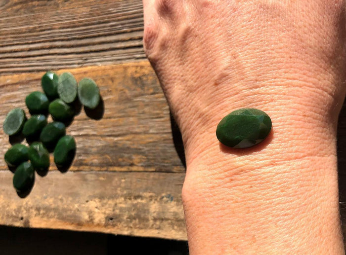 Single dark green 13x18 mm faceted oval cabochon on a forearm for size reference.