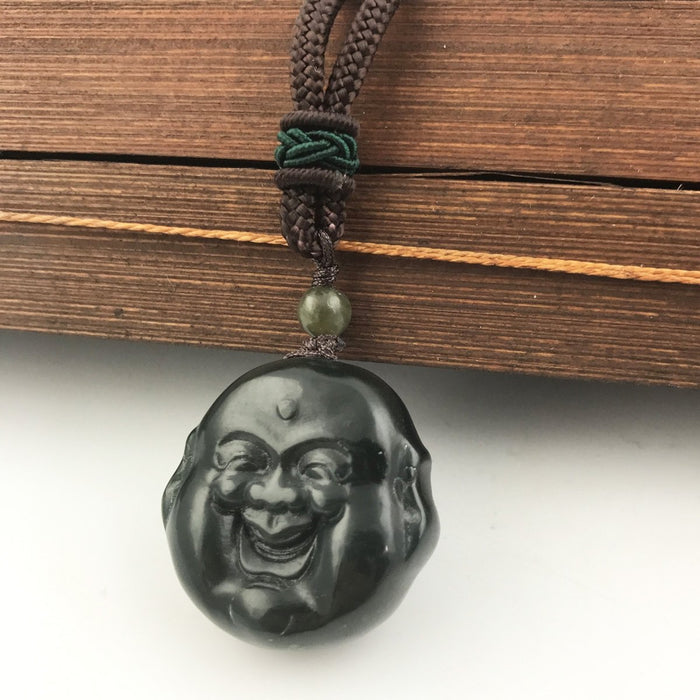 Circular black Buddha head pendant with a carved laughing face on a brown braided cord necklace with a green bead above.