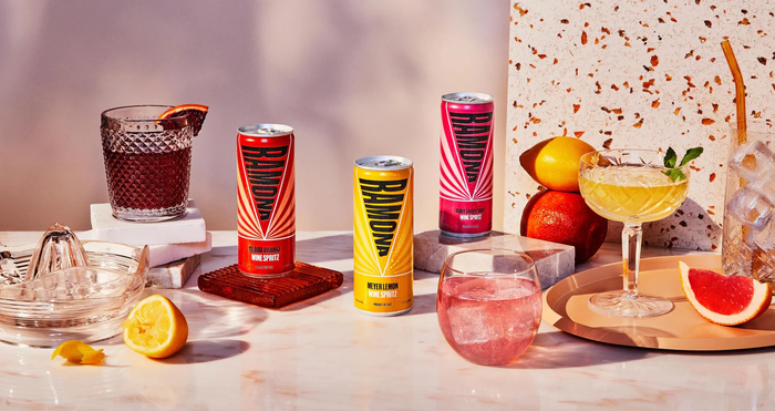 Set of pink grapefruit spritz cans on table with citrus slices and glass