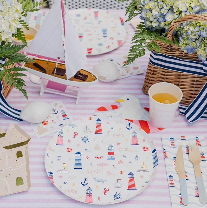 Nautical-themed table setting with plates, cups, and decor on a striped tablecloth.
