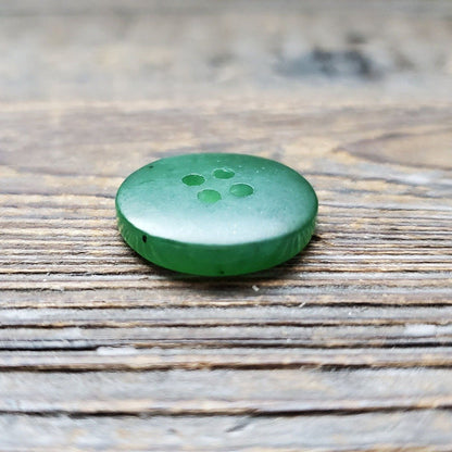 Green jade button with four holes on a weathered wooden surface