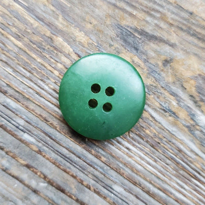 Top-down view of a green jade button with four holes on a textured wooden surface