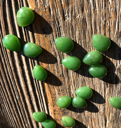 Group of bright green pear shaped cabochons scattered on a rustic wooden surface