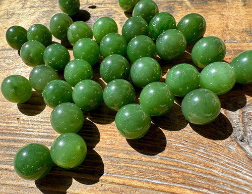A+ Half Drilled 10mm Canadian Jade beads scattered on a sunlit wooden surface