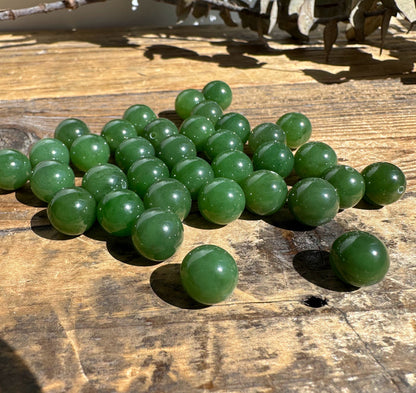 A+ Half Drilled 10mm Canadian Jade beads clustered on a sunlit wooden surface