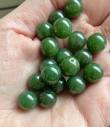 Polished green jade beads held in a palm, showing 10mm half drilled Canadian Jade beads