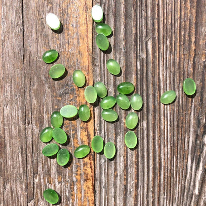Green jade cabochons 5x7 mm scattered on a weathered wooden surface.