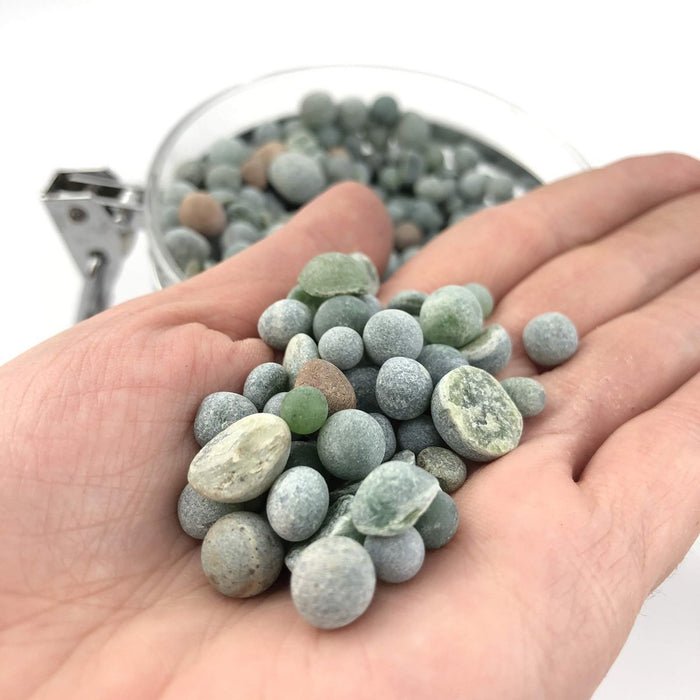 Small green and gray aquarium beads held in an open hand with a bead filled bowl in the background