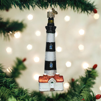 A lighthouse-shaped Christmas ornament with black and white stripes hangs on a green Christmas tree, with soft, blurred white lights glowing in the background.