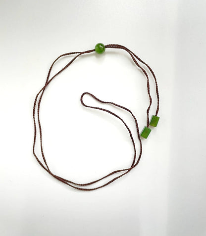 Brown braided cord necklace featuring a single round jade bead and two square jade beads