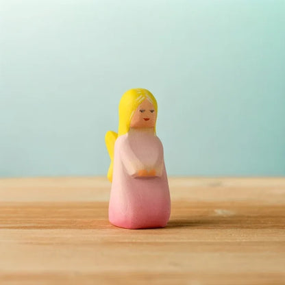 Small figurine of a person with yellow hair and pink body on a wooden surface with a light blue background