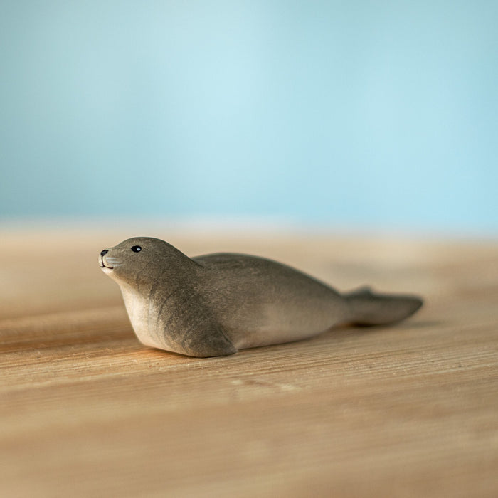 A small realistic seal figurine lying on a light wooden surface with a soft blue background.