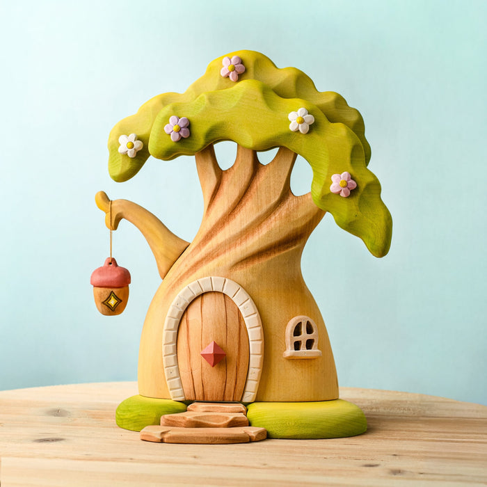 Wooden fairy house with a green roof and pink flowers on a light blue background