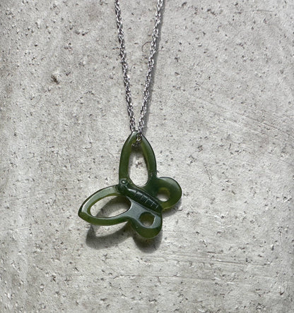 Green butterfly pendant with a silver chain on a textured gray background.