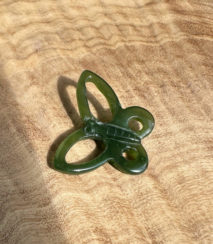 Green butterfly pendant on brown textured fabric background.