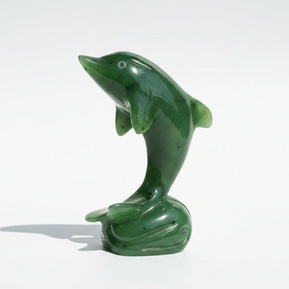 A polished green jade-like dolphin figurine standing on a small base, photographed on a wooden surface against a light neutral backdrop.