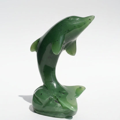 A polished green jade dolphin figurine standing on a wooden surface against a neutral light background.