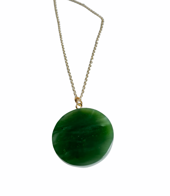 Round Canadian jade evil eye pendant in deep green suspended from a gold bail on a silver chain
