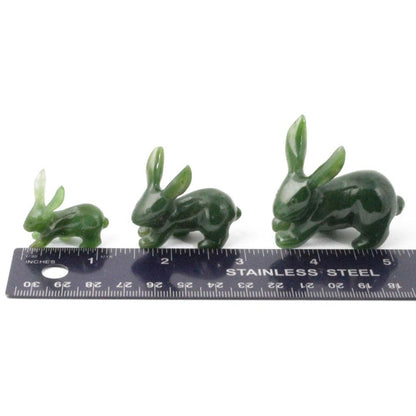 Three green jade jackrabbit carvings arranged by size beside a stainless steel ruler