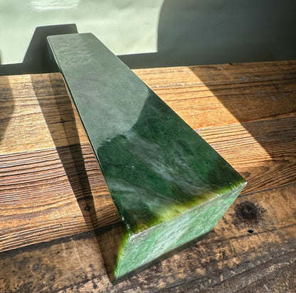 Canadian Jade Obelisk resting diagonally on a rustic wooden surface, deep green with a lighter base.