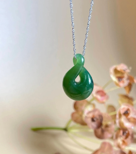 Cassiar jade infinity twist pendant on a silver chain against a soft background.