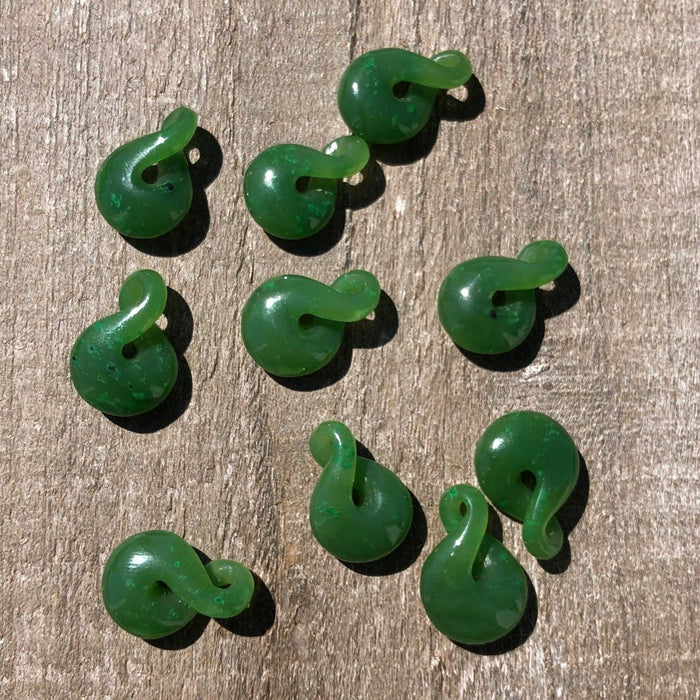 Several small green jade infinity twist beads scattered on a wood surface