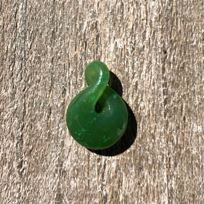 Single green jade infinity twist pendant resting on a wooden surface
