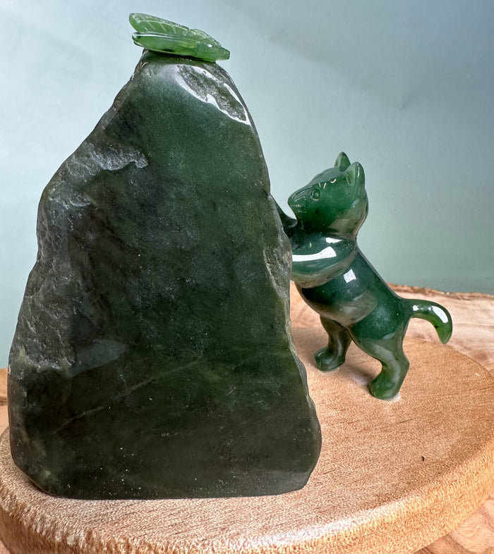 Green jade cat pawing at a small jade butterfly perched on a dark rock.