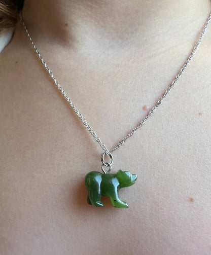 A close-up of a person's neck and chest wearing a silver chain necklace with a small carved green bear pendant.