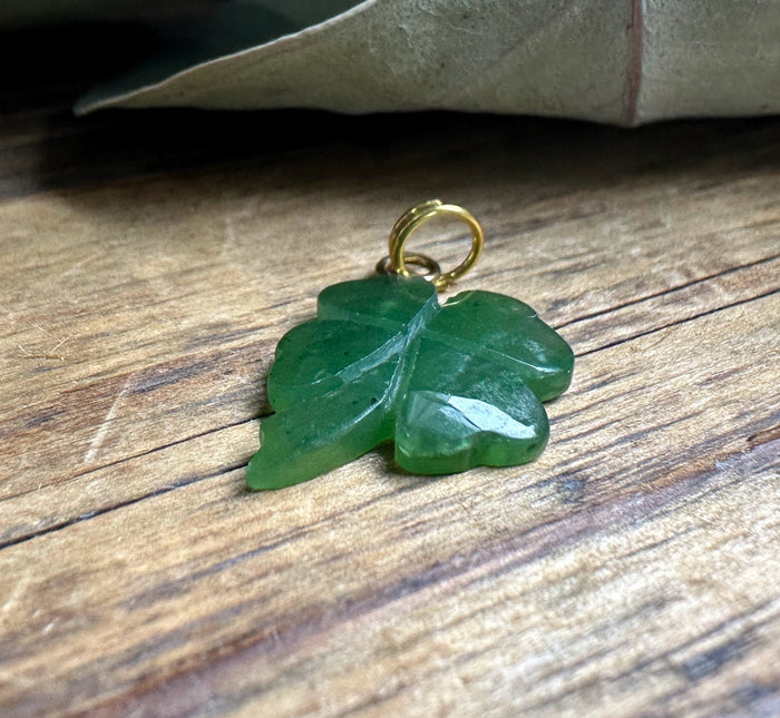 Close-up of green shamrock charm with a gold loop on a wood background.