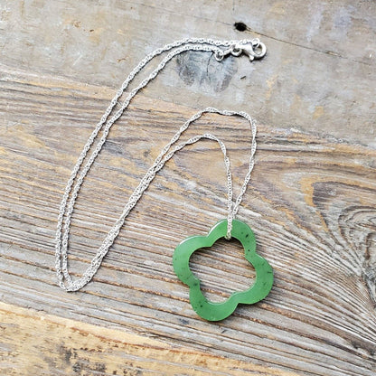 Green clover pendant on a silver chain laid on a wooden surface.