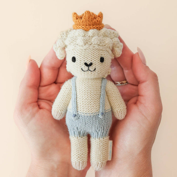 Knitted toy sheep with a crown held in a hand against a beige background