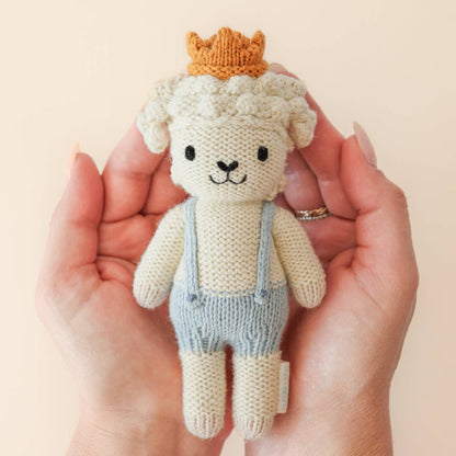 Knitted toy sheep with a crown held in a hand against a beige background