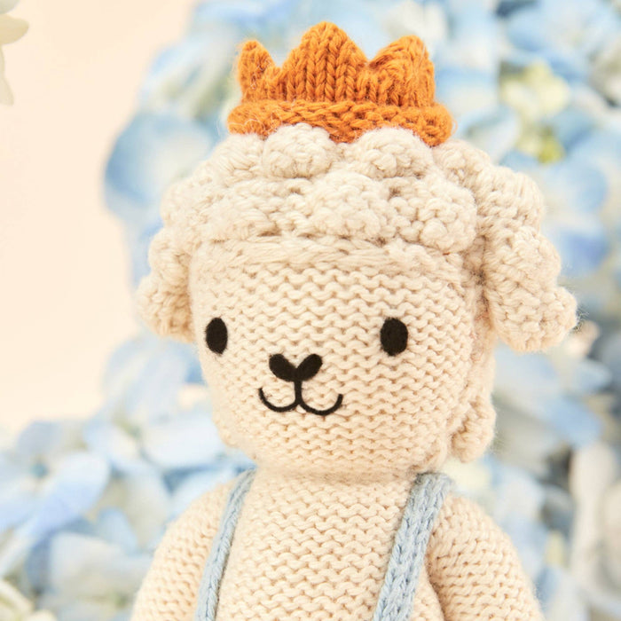 Knitted toy sheep with a crown against a blurred natural background