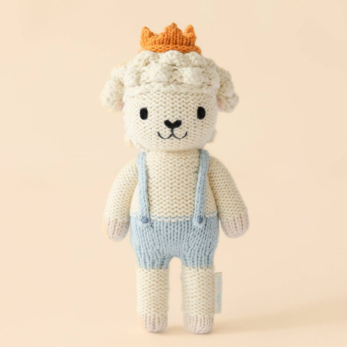 Knitted toy sheep with a crown and overalls on a beige background