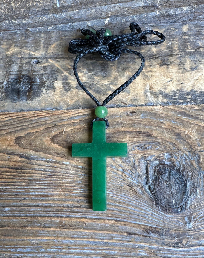 Dark green jade cross pendant on a black braided cord tied into a heart shape with a green bead above the pendant