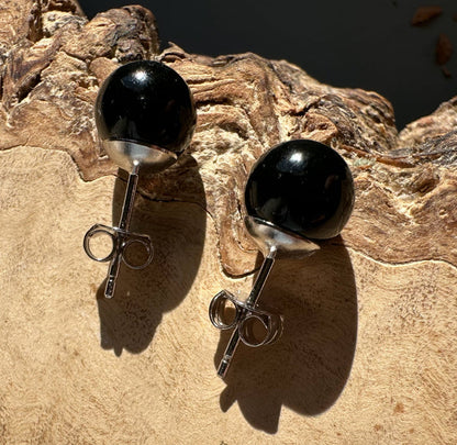 Pair of black jade sphere stud earrings with silver posts on a textured rock surface