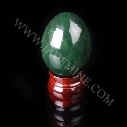 Polished green gemstone egg perched on a glossy red stand against a black background.