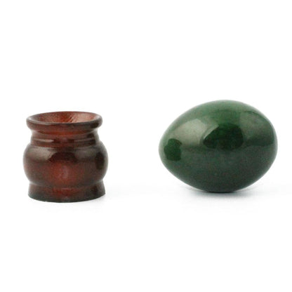 Small brown ceramic jar beside a glossy dark green egg on a white background.