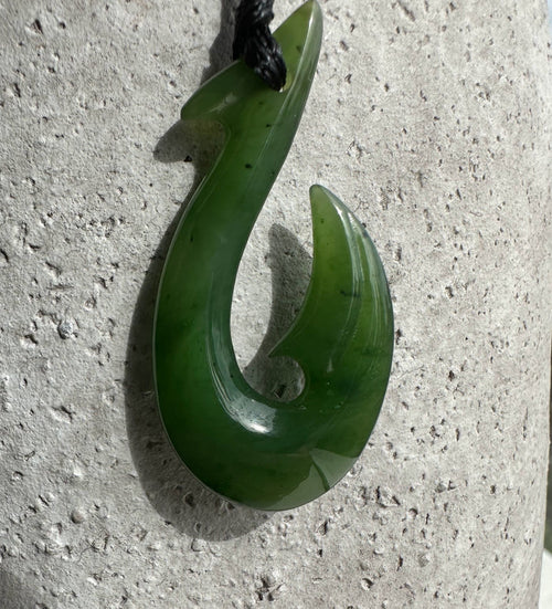 Green jade fish hook pendant with a curved hook design on a black cord