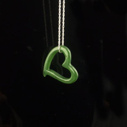 Emerald green heart shaped pendant on a silver chain against a black background.