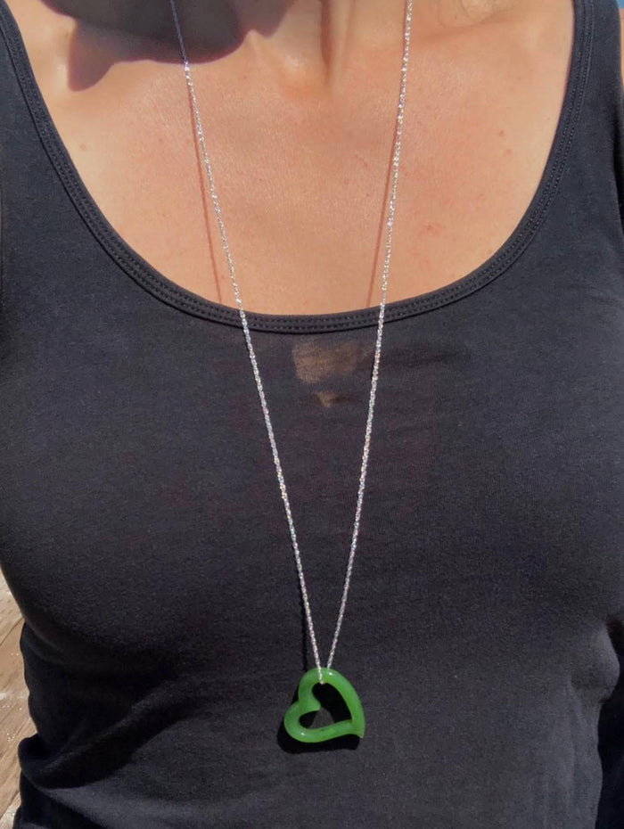Green heart shaped pendant on a silver chain worn over a black tank top.