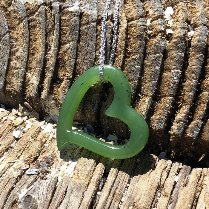 Green heart shaped pendant on a silver chain laid against weathered wood background.