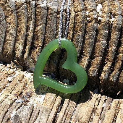 Green heart shaped pendant on a silver chain laid against weathered wood background.