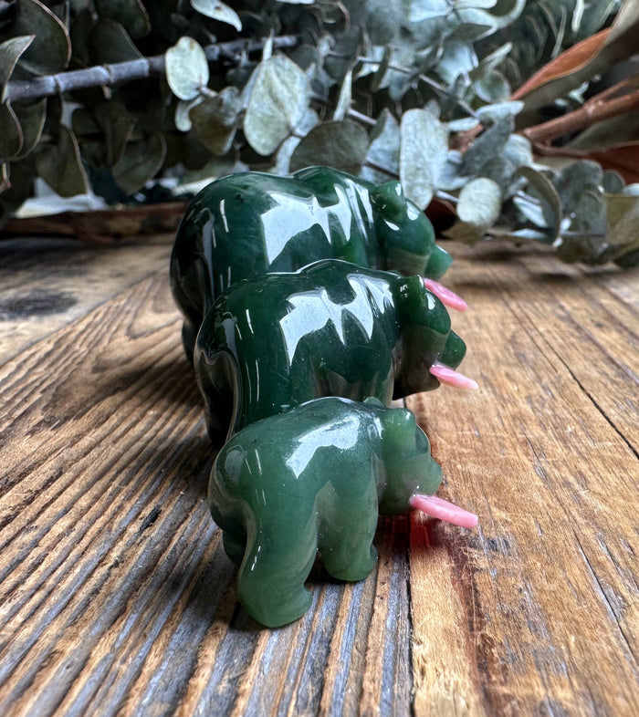 Three dark green jade bears with pink rhodonite fish protruding from their mouths on a rustic wood surface