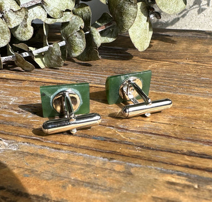 Back view of green jade cufflinks with silver toggle bars on a wood surface.