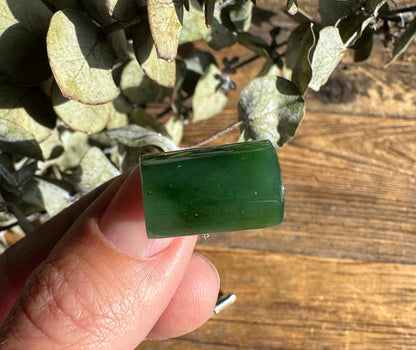 Close up of green jade rectangular piece held between fingers over a wooden surface.